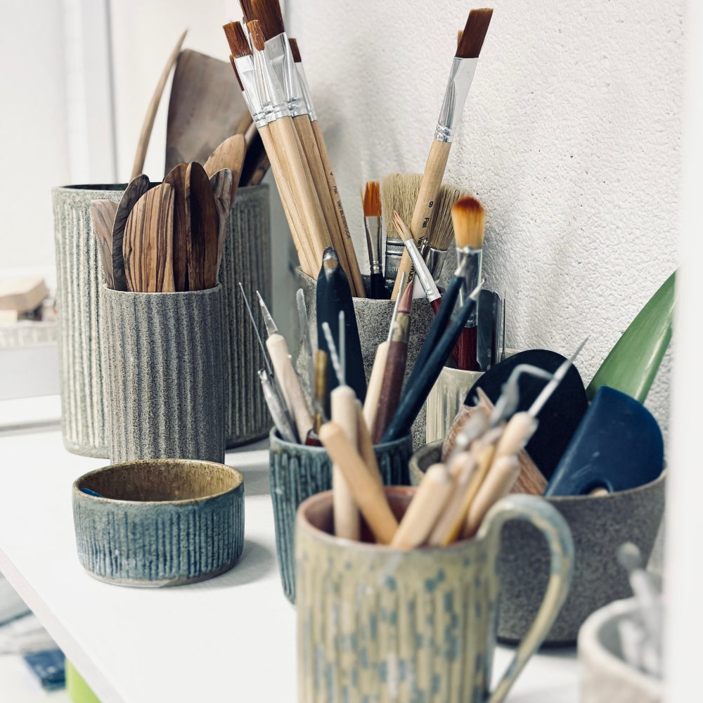 Collection of paintbrushes in ceramic holders on a white surface